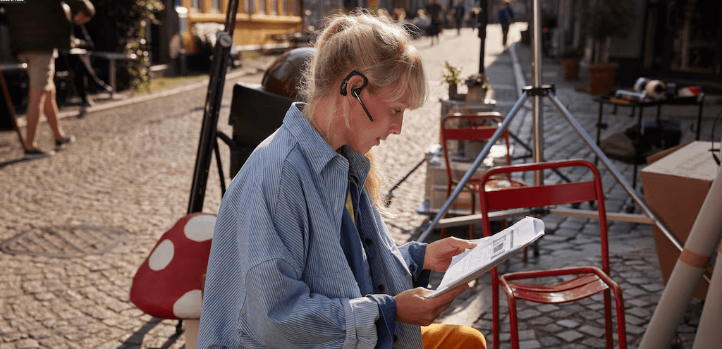 Profissional usando fones de ouvido Bluetooth enquanto l&ecirc; documentos em um caf&eacute; ao ar livre