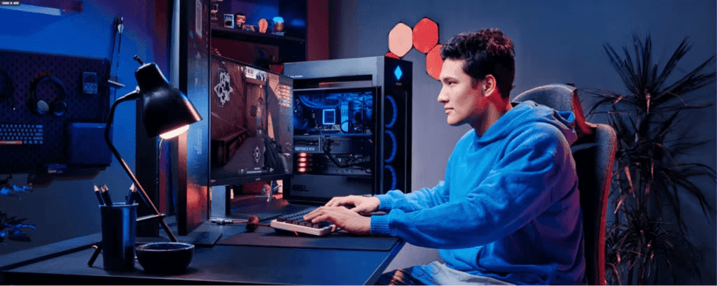 Uma pessoa em um moletom azul sentada em frente a uma configura&ccedil;&atilde;o de jogos com um gabinete de PC aberto exibindo componentes internos, iluminado por luzes azuis e vermelhas em uma sala escura com decora&ccedil;&otilde;es de parede hexagonais